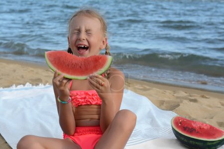Foto de Linda niña comiendo jugosa sandía en la playa - Imagen libre de derechos