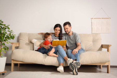 Photo for Happy family reading book together on sofa in living room at home - Royalty Free Image