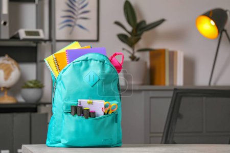 Turquoise backpack with different school stationery on table indoors, space for text