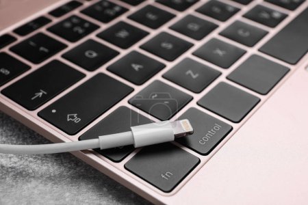 Téléchargez les photos : Câble USB avec connecteur Lightning et ordinateur portable sur table grise, gros plan - en image libre de droit