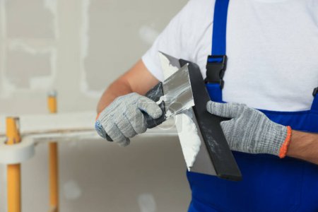 Photo for Worker with putty knives and plaster near wall, closeup - Royalty Free Image