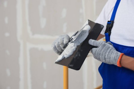 Photo for Worker with putty knives and plaster near wall, closeup. Space for text - Royalty Free Image