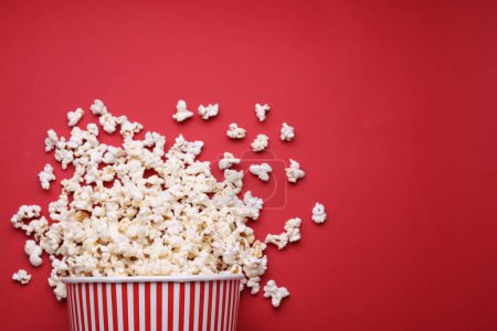 Photo for Overturned paper bucket with delicious popcorn on red background, flat lay. Space for text - Royalty Free Image