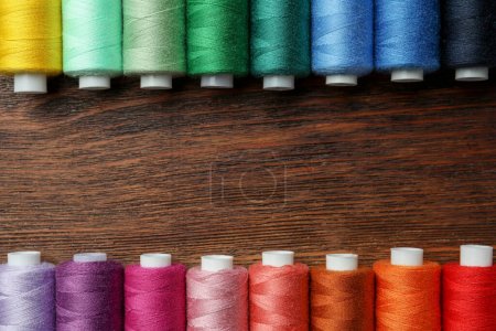 Frame of colorful sewing threads on wooden table, flat lay. Space for text