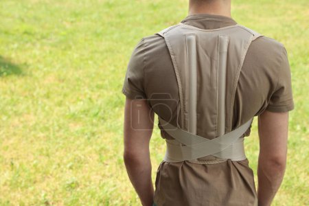 Photo for Closeup of man with orthopedic corset on green grass outdoors, back view. Space for text - Royalty Free Image