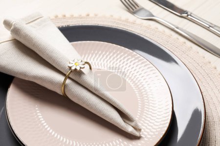 Assiettes avec serviette en tissu, anneau décoratif et couverts sur table en bois blanc