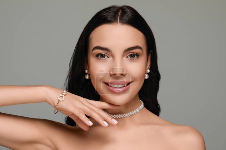 Téléchargez les photos : Jeune femme portant des bijoux de perles élégantes sur fond gris - en image libre de droit
