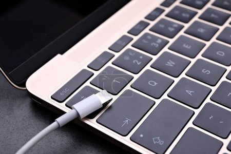 Téléchargez les photos : Câble USB avec connecteur Lightning et ordinateur portable sur table noire, gros plan - en image libre de droit