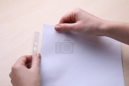 Foto de Mujer poniendo hoja de papel en el bolsillo perforado en la mesa de madera, primer plano - Imagen libre de derechos