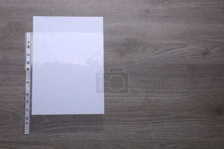 Punched pocket with paper sheet on wooden table, top view. Space for text