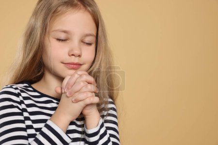 Foto de Chica con las manos apretadas rezando sobre fondo beige, espacio para el texto - Imagen libre de derechos
