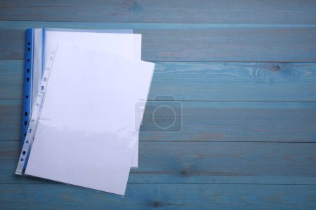 Foto de Carpeta de archivo con bolsillos perforados y hojas de papel sobre mesa de madera azul claro, disposición plana. Espacio para texto - Imagen libre de derechos