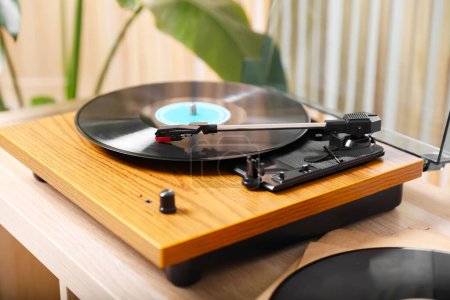 Elegante tocadiscos con disco de vinilo en mesa de madera ligera en el interior