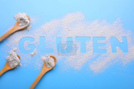 Löffel und Wort Gluten geschrieben mit Mehl auf hellblauem Hintergrund, flache Lage