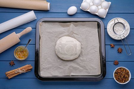 Téléchargez les photos : Plat à pâtisserie avec pâte, papier sulfurisé et ingrédients sur table en bois bleu, plat - en image libre de droit