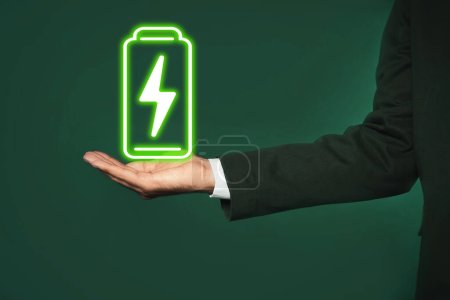 Businessman demonstrating at icon of charging battery on color background, closeup