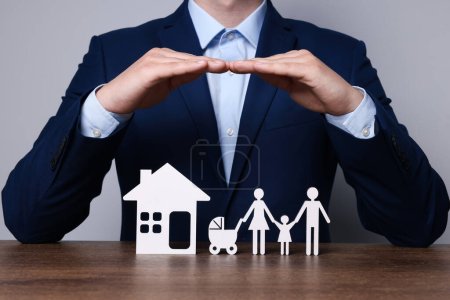 Photo for Man protecting figures of family and house at wooden table. closeup. Insurance concept - Royalty Free Image