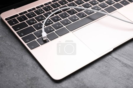 Téléchargez les photos : Câble USB avec connecteur Lightning et ordinateur portable sur table grise, gros plan - en image libre de droit