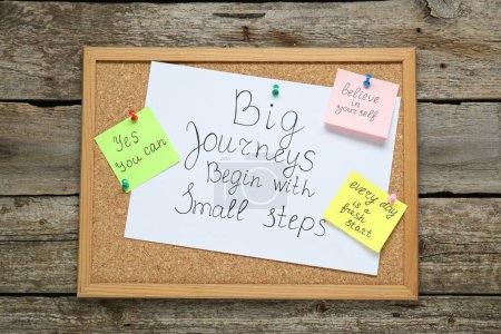 Corkboard with motivational quotes on wooden table, top view