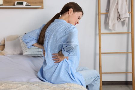 Téléchargez les photos : Femme souffrant de maux de dos alors qu'elle était assise sur son lit à la maison. Symptôme de scoliose - en image libre de droit