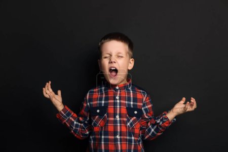 Photo for Angry little boy screaming on black background. Aggressive behavior - Royalty Free Image