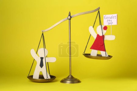Photo for Gender pay gap. Wooden figures of man and woman on scales against yellow background - Royalty Free Image