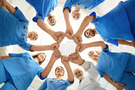 Photo for Doctor and interns holding fists together indoors, bottom view - Royalty Free Image
