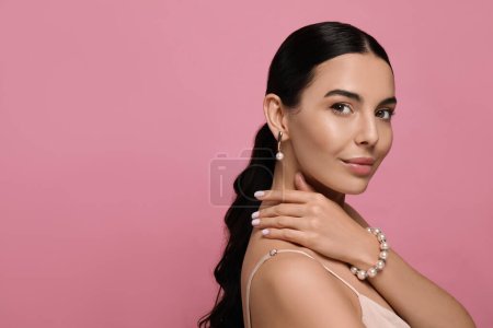 Téléchargez les photos : Jeune femme portant des bijoux de perles élégantes sur fond rose, espace pour le texte - en image libre de droit