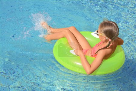 Téléchargez les photos : Petite fille mignonne avec anneau gonflable dans la piscine le jour ensoleillé - en image libre de droit