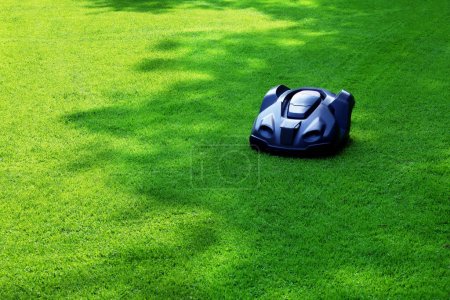 Foto de Modern robot lawn mower on green grass in garden - Imagen libre de derechos