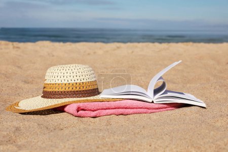 Photo for Open book, hat and pink towel on sandy beach near sea - Royalty Free Image