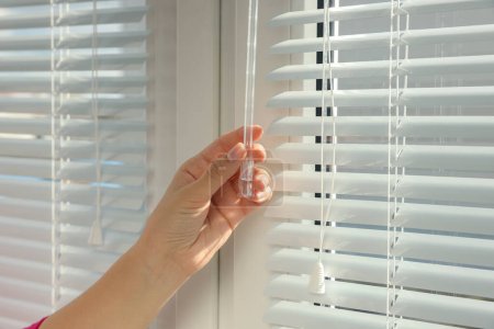 Photo for Woman opening horizontal blinds on window indoors, closeup - Royalty Free Image