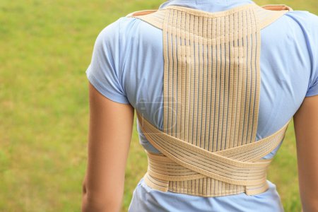 Photo for Closeup of woman with orthopedic corset on green grass outdoors, back view - Royalty Free Image