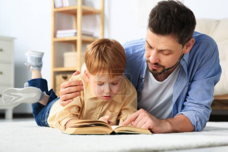 Téléchargez les photos : Père lisant le livre avec son fils sur le sol dans le salon à la maison - en image libre de droit
