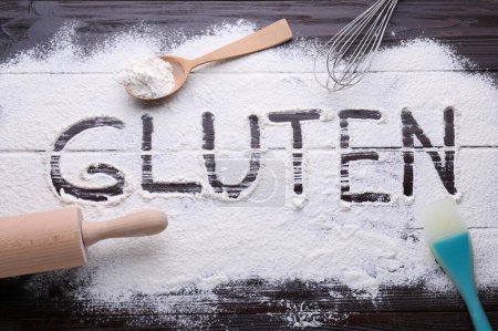 Photo for Kitchen utensils and word Gluten written with flour on dark wooden table, flat lay - Royalty Free Image
