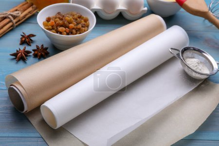 Téléchargez les photos : Rouleaux de papier sulfurisé, différents ingrédients et outils de cuisine sur table en bois bleu clair - en image libre de droit