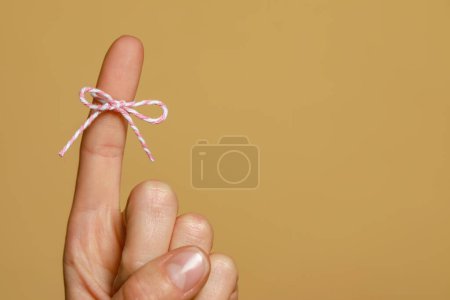 Photo for Woman showing index finger with tied bow as reminder on light brown background, closeup. Space for text - Royalty Free Image