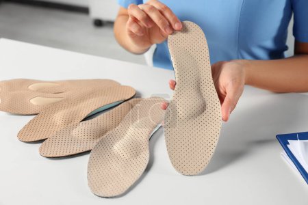 Female orthopedist showing insoles at table in hospital, closeup