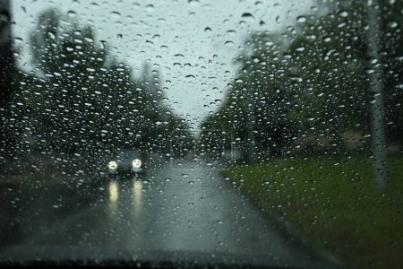 Téléchargez les photos : Vue floue de la route à travers la fenêtre de la voiture mouillée. Météo pluvieuse - en image libre de droit