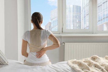Photo for Woman with orthopedic corset sitting in bedroom, back view - Royalty Free Image