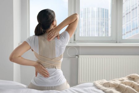Téléchargez les photos : Femme avec corset orthopédique assis dans la chambre, vue arrière - en image libre de droit