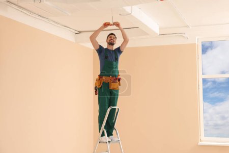 Photo for Electrician in uniform with pliers repairing ceiling wiring indoors - Royalty Free Image