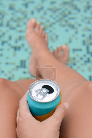 Woman holding aluminum can with beverage near swimming pool, closeup