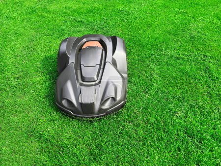 Foto de Modern robot lawn mower on green grass in garden - Imagen libre de derechos