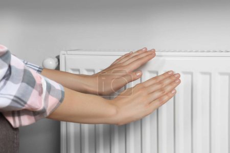 Photo for Woman warming hands on heating radiator near white wall, closeup - Royalty Free Image