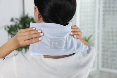 Mujer usando almohadilla de calefacción en el cuello en casa, primer plano