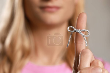 Woman showing index finger with tied bow as reminder against blurred background, focus on hand