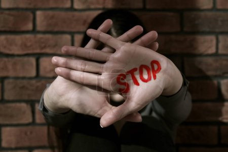 Foto de Concepto de violencia doméstica. Mujer escondiendo su cara, concéntrate en las manos con la palabra escrita Stop - Imagen libre de derechos