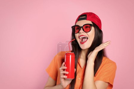 Foto de Mujer joven emocionada en gafas de sol elegantes que sostienen lata con bebida sobre fondo rosa. Espacio para texto - Imagen libre de derechos