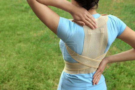 Closeup of woman with orthopedic corset on green grass outdoors, back view. Space for text